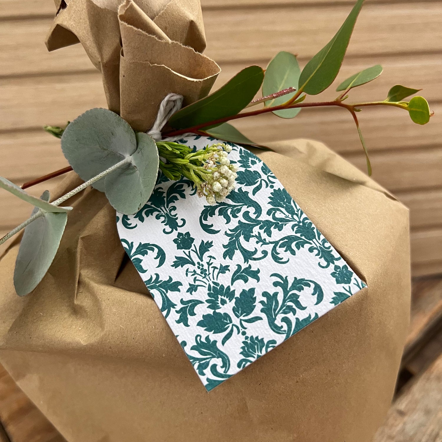 Gift wrapped in brown paper with a plantable tag and greenery on a wooden surface