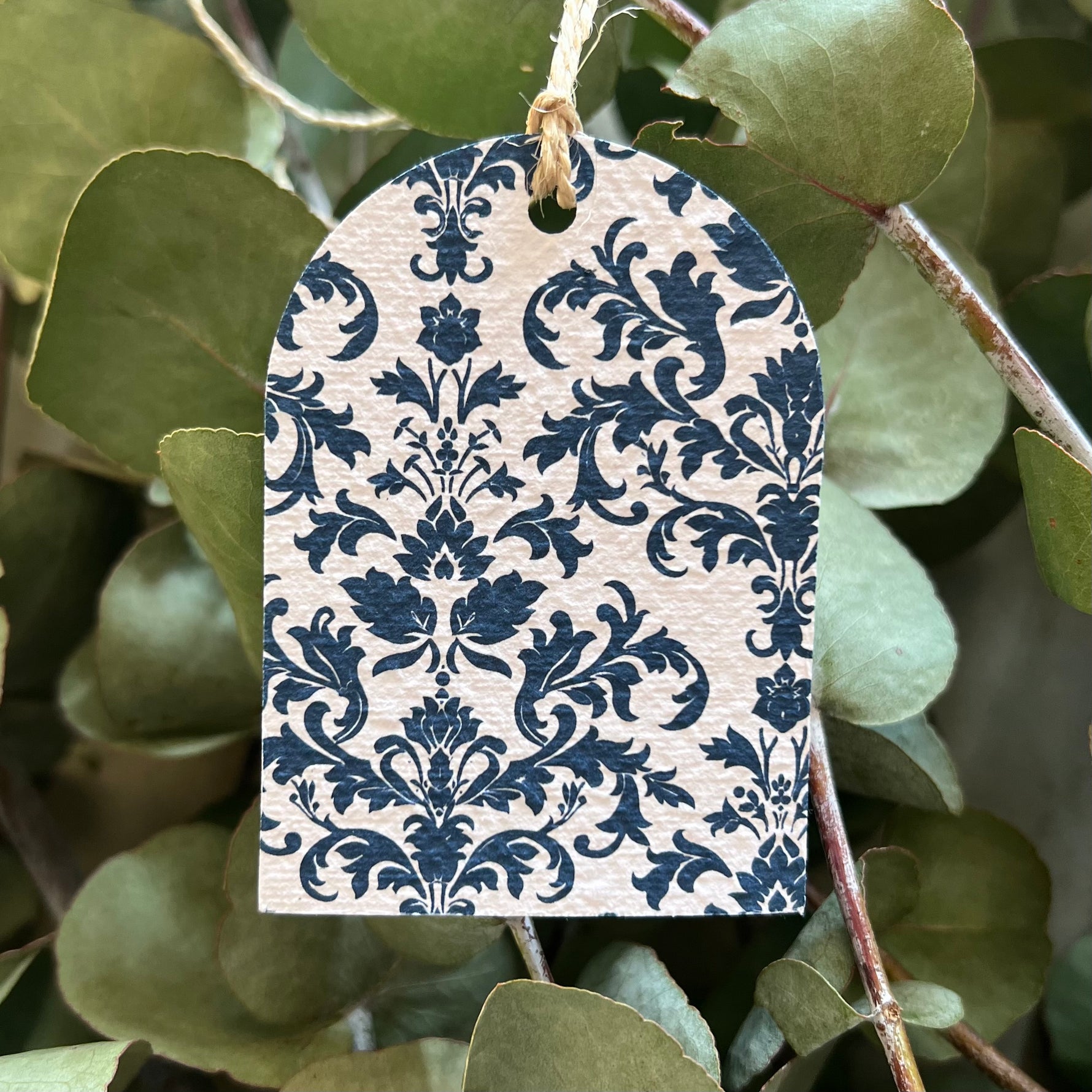 Plantable tag with blue floral pattern hanging among green leaves