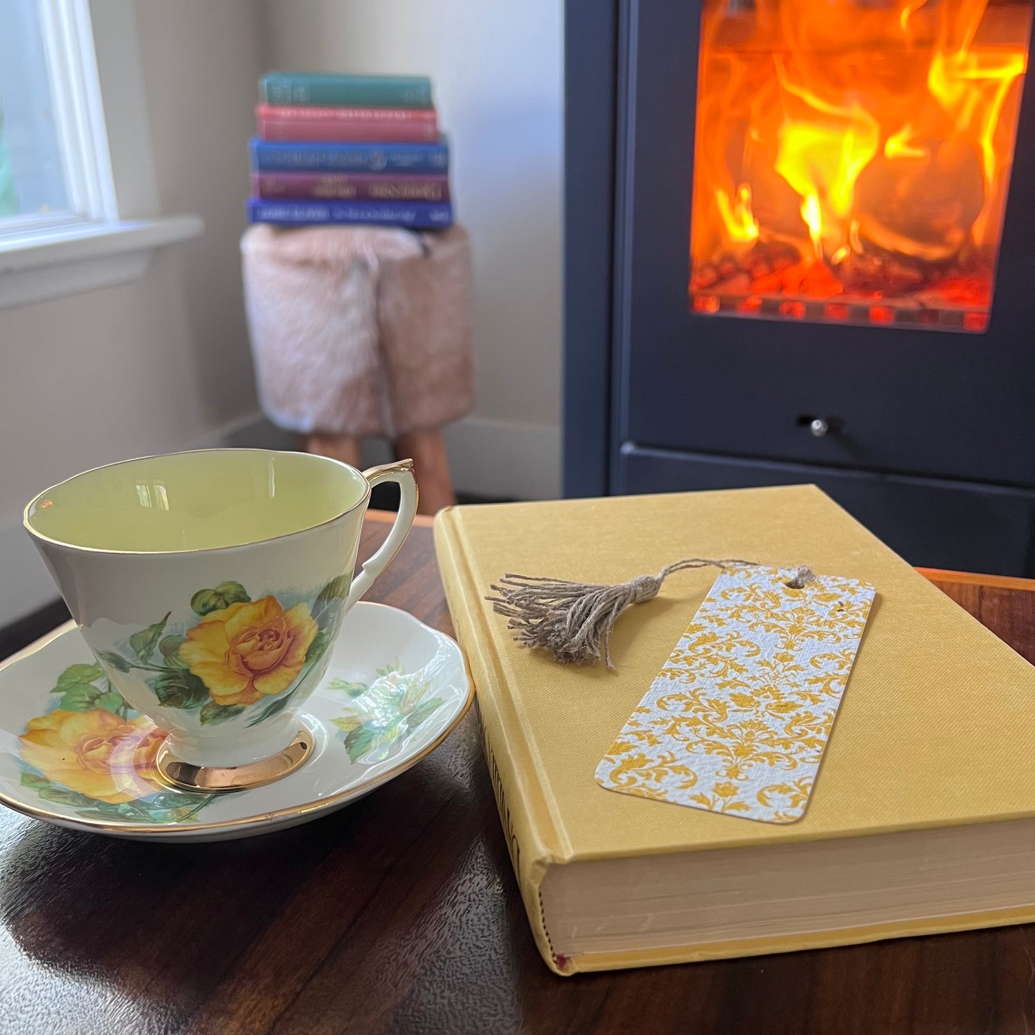 Teacup and saucer with a book and plantable bookmark on a table in front of a fireplace.