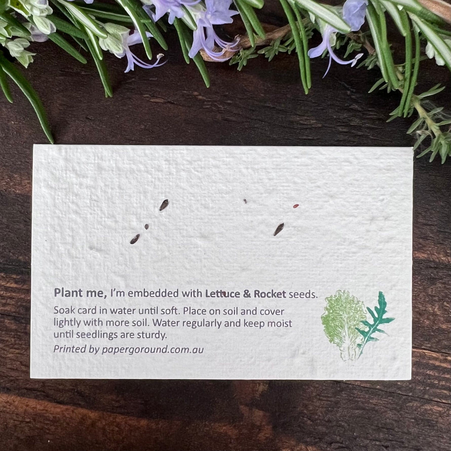 Seed paper card with lettuce and rocket seeds on a wooden surface.