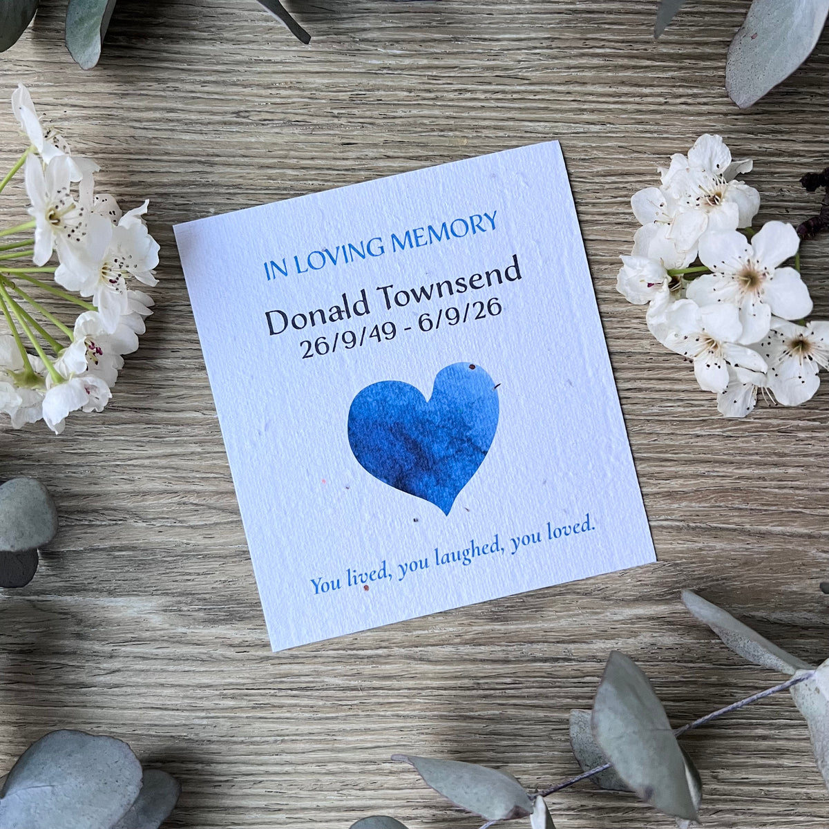 Seed paper memorial card with blue text and a blue heart illustration.